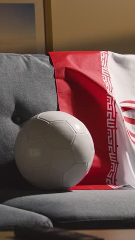 Vertikales-Video-Eines-Sofas-In-Der-Lounge-Mit-Iranischer-Flagge-Und-Ball,-Während-Sich-Fans-Darauf-Vorbereiten,-Fußballspiele-Im-Fernsehen-Zu-Sehen